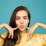 portrait photo of woman in yellow t shirt posing with her fingers on her cheeks