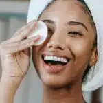 ethnic smiling woman wiping face with cotton pad