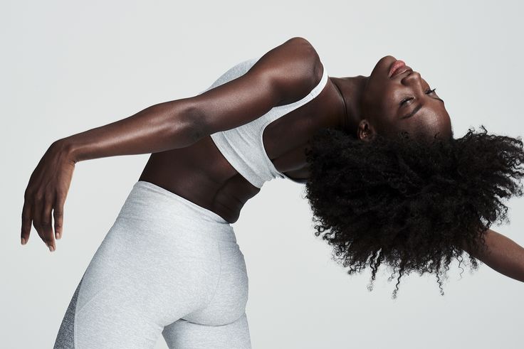 A woman in motion, gracefully bending backward in a yoga-inspired pose, wearing light gray activewear against a minimalist background. Showcasing strength and flexibility as part of a wellness routine.