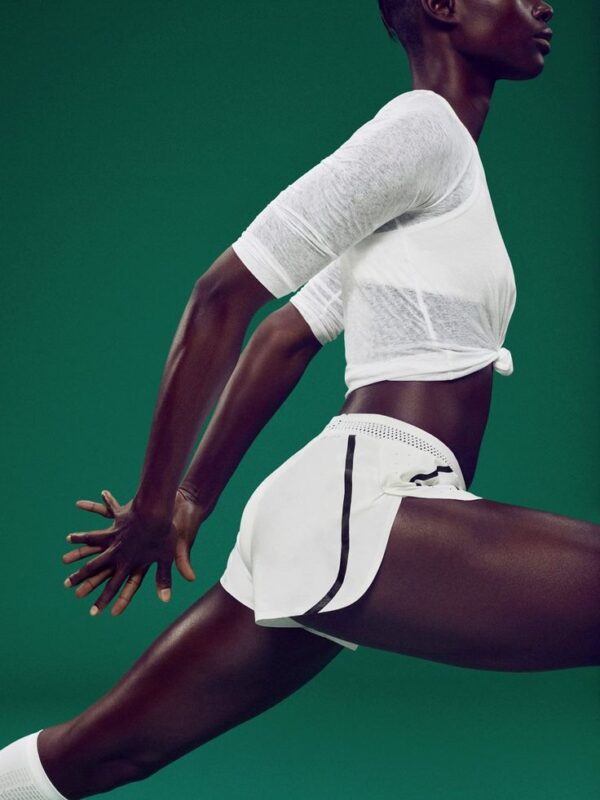 A woman stretching dynamically in a white athletic top and shorts against a vibrant green background. A depiction of an active and energized approach to wellness and fitness.